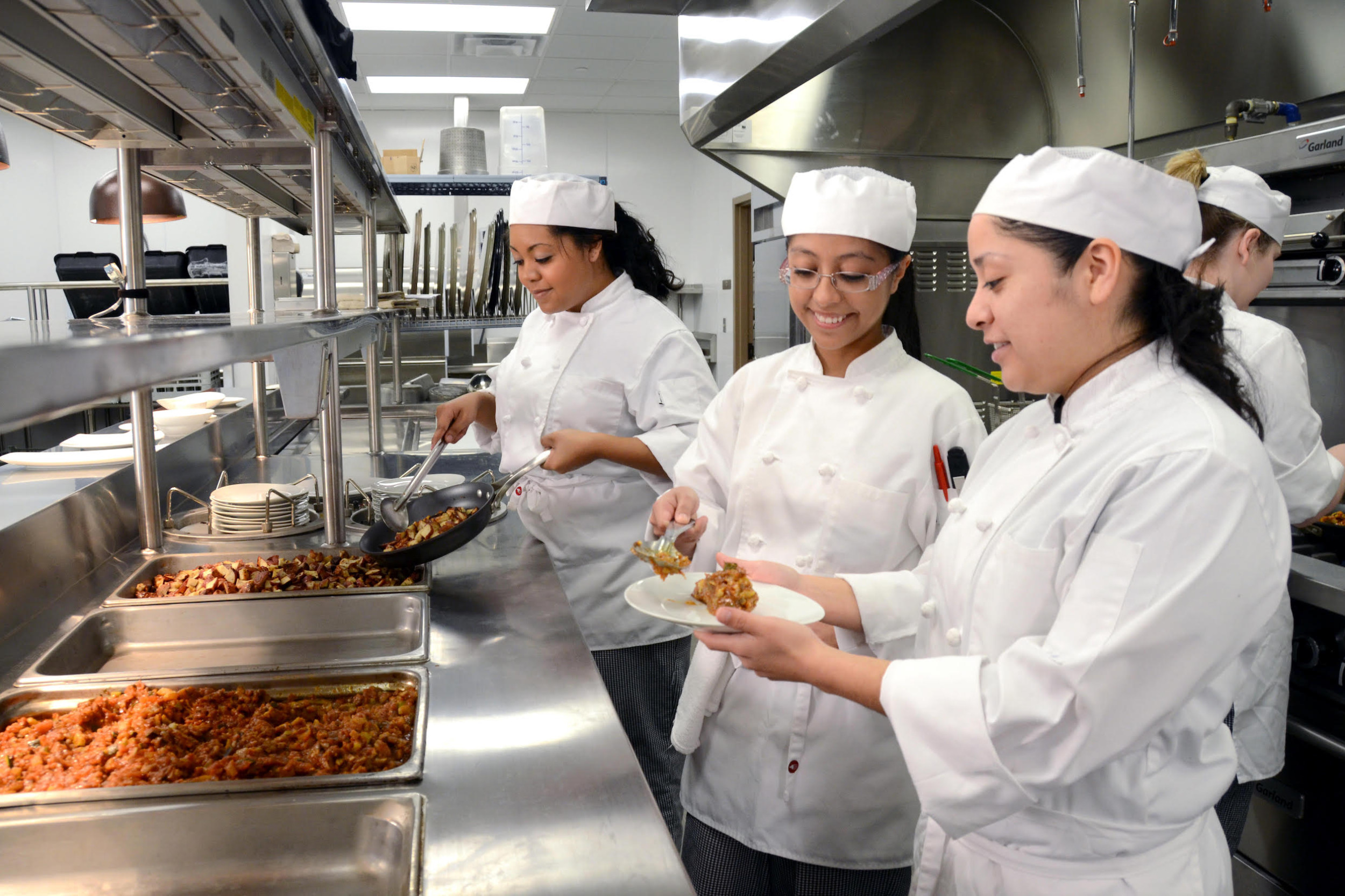 Ladies in a commercial kitchen cooking and preparing a plate